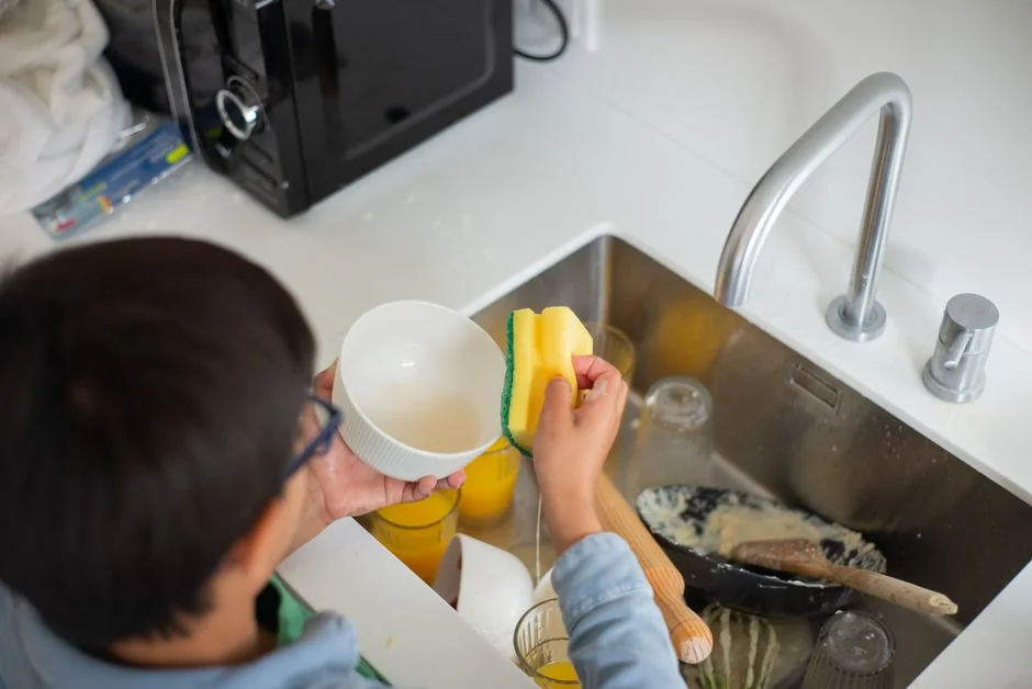 Gros plan d’une main nettoyant une fenêtre avec une raclette en extérieur, avec des gants jaunes.