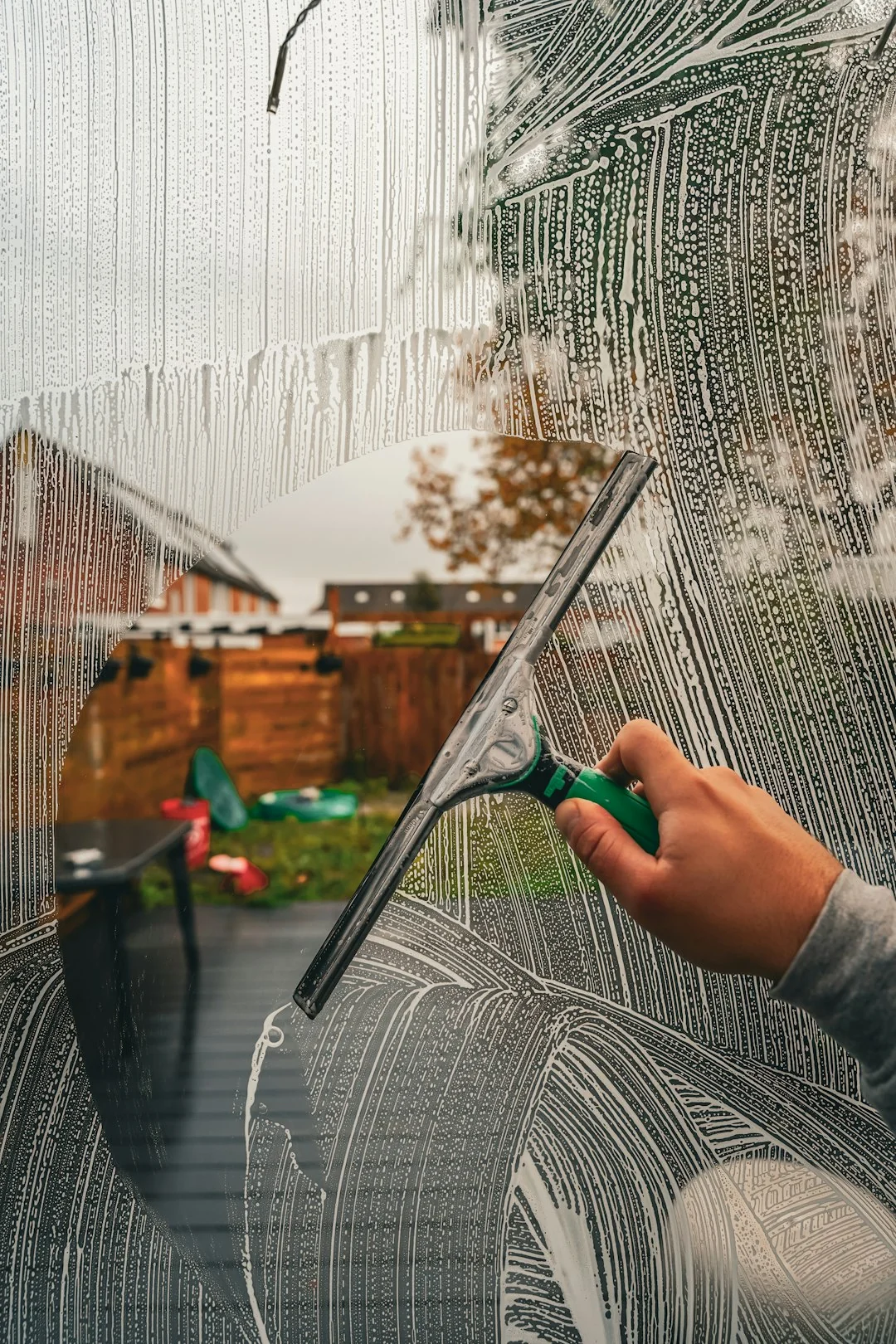 A man cleaning a glass barrier outdoors with a squeegee, surrounded by greenery.